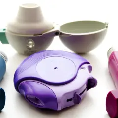 Drei Inhalatoren in Lila, Blau und Pink, sowie ein offener weißer Inhalator. Ein Beispiel für Medikamente wie Spiriva.