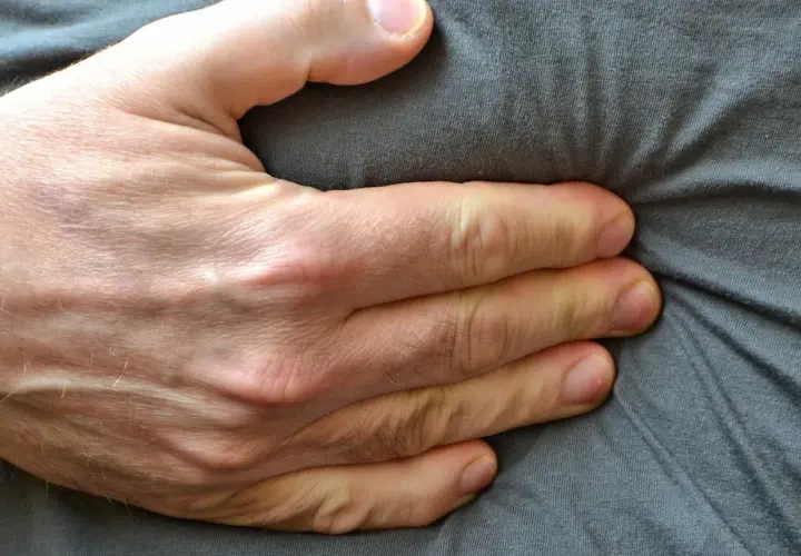 Eine Hand drückt auf den Bauch, was auf Beschwerden wie bei einer Lebensmittelunverträglichkeit hindeuten könnte.