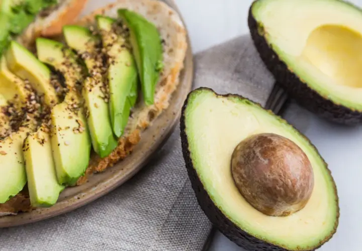 Avocado-Toast mit Gewürzen und frischem Basilikum. Ist Avocado Obst oder Gemüse? Botanisch ist sie eine Frucht, kulinarisch oft als Gemüse verwendet.