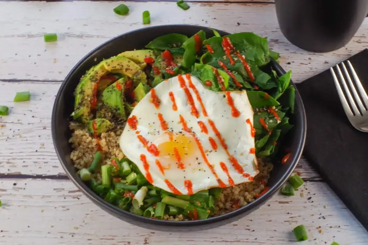 Schüssel mit Quinoa, Spinat, Spiegelei und geschnittenem Avocado. Ein gesundes Frühstück, das Energie gibt.