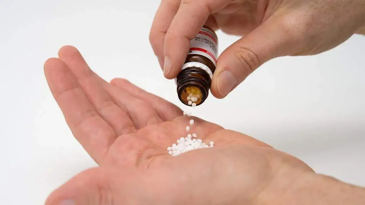 Eine Hand schüttet kleine weiße Globuli aus einer Flasche in die andere Hand.