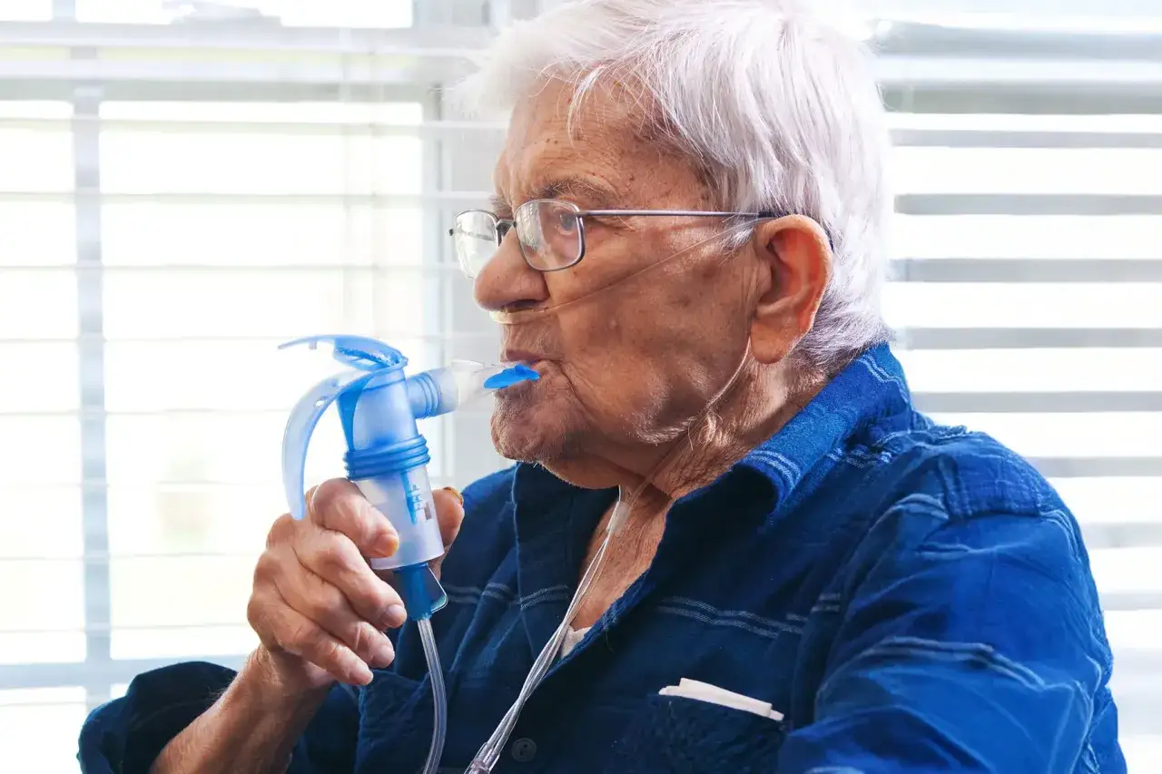 Älterer Mann mit Brille und Nasenbrille nutzt ein Inhalationsgerät, um Medikamente wie Spiriva zu atmen.