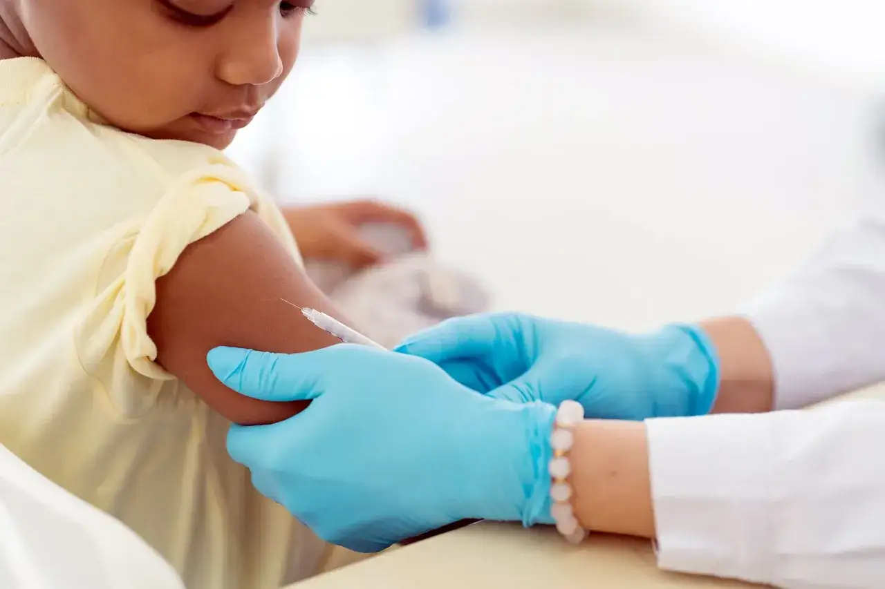 Kind erhält Impfung mit Boostrix Polio. Arzt mit blauen Handschuhen injiziert.